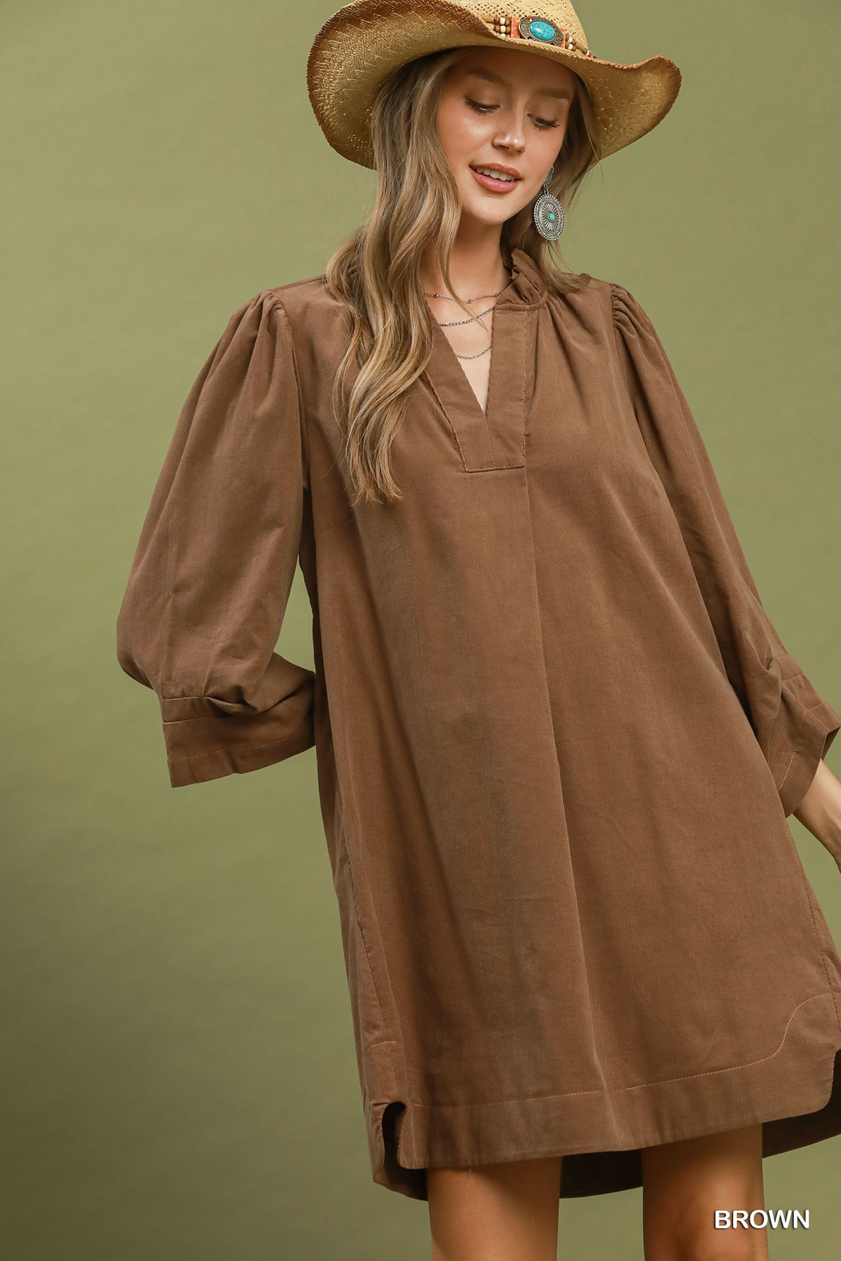 Woman wearing a brown corduroy split neck shift dress with puff sleeves and a straw hat.