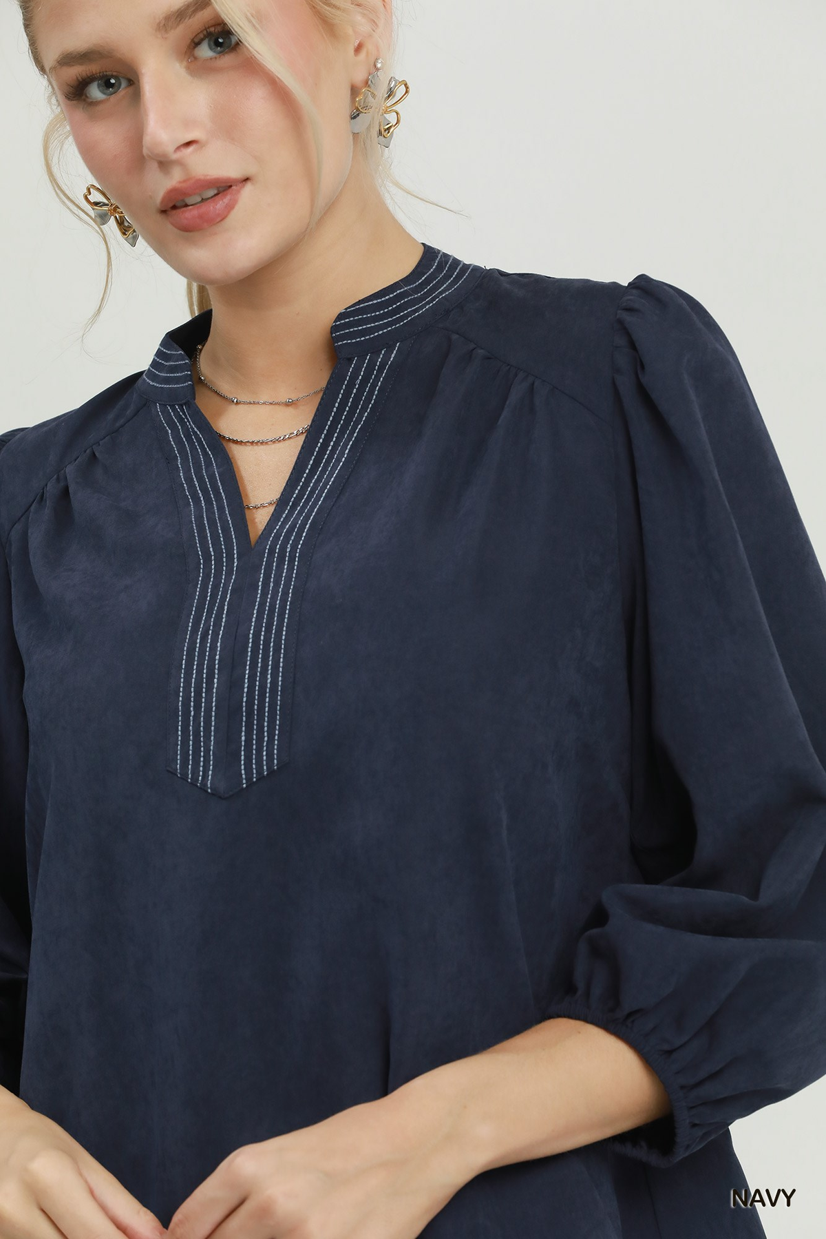 Close-up of a navy sueded split neck blouse with white contrast stitching and puff sleeves.