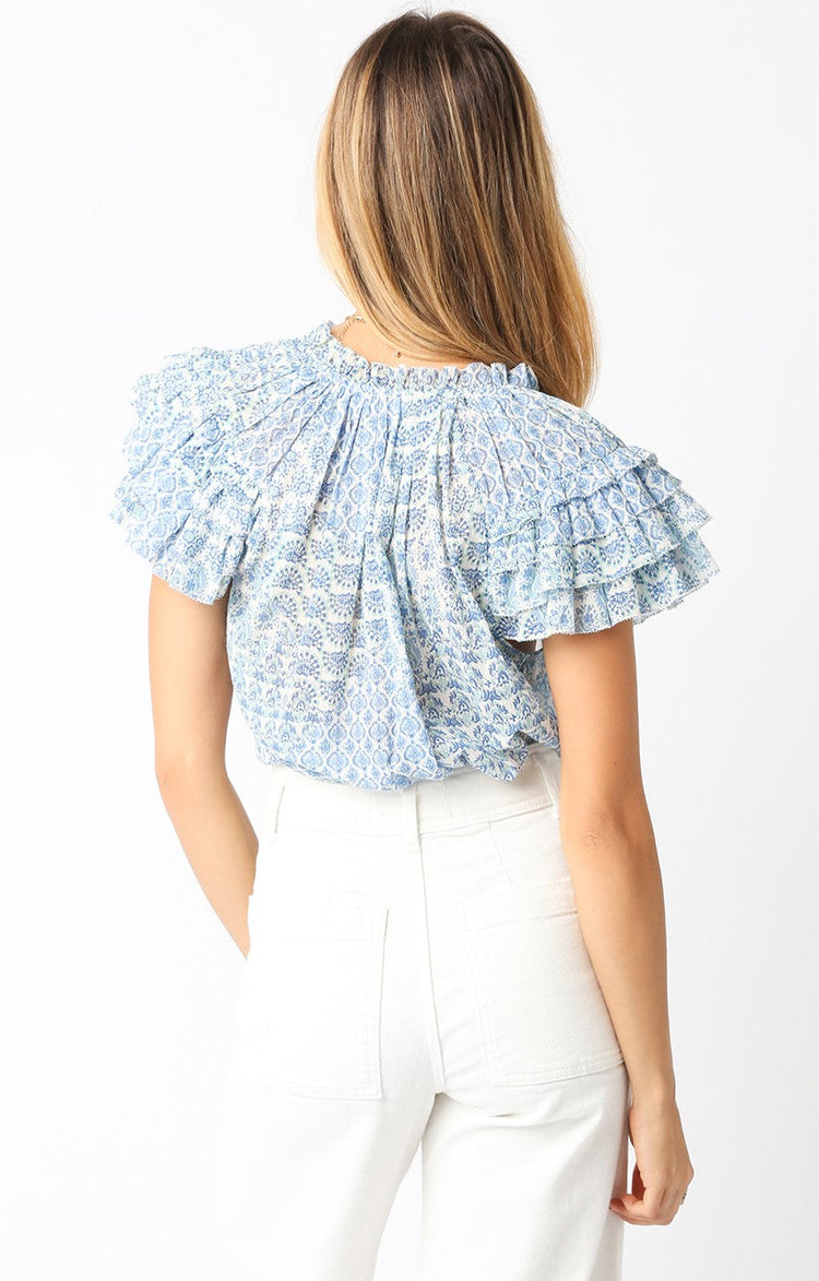 Back view of a woman wearing the Louise Top, a blue and white patterned blouse with ruffled sleeves.