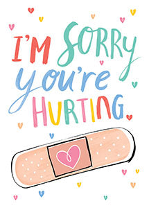 A greeting card with the words "I'm sorry you're hurting" in colorful script, featuring a band-aid with a pink heart.