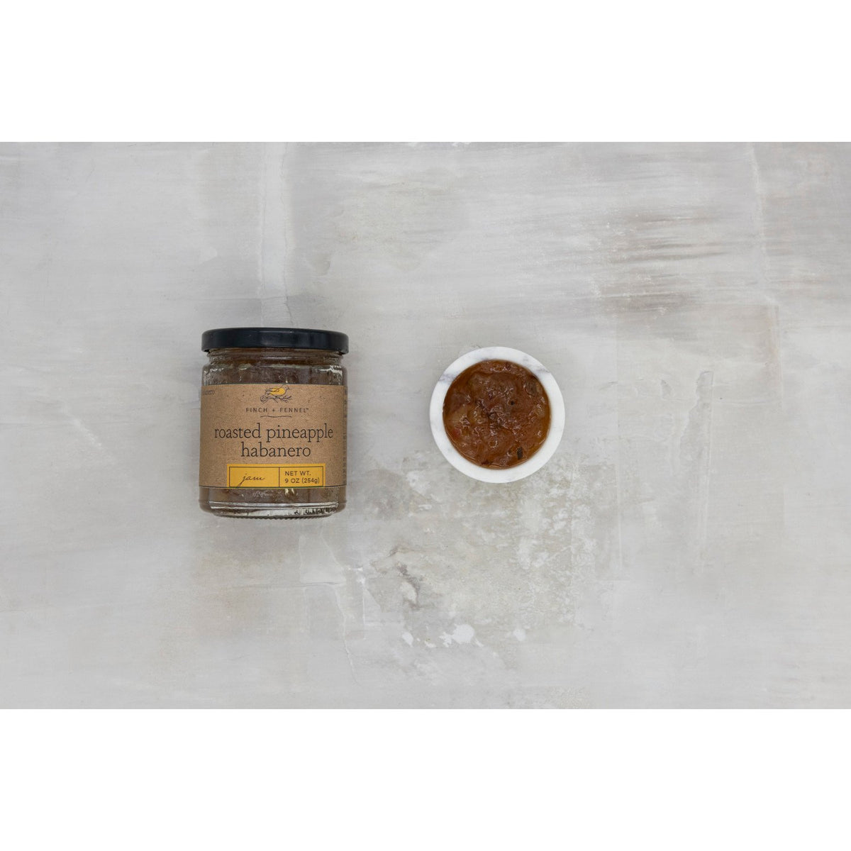 A 9 oz jar of Finch + Fennel Roasted Pineapple Habanero Jam next to a small bowl of the jam.