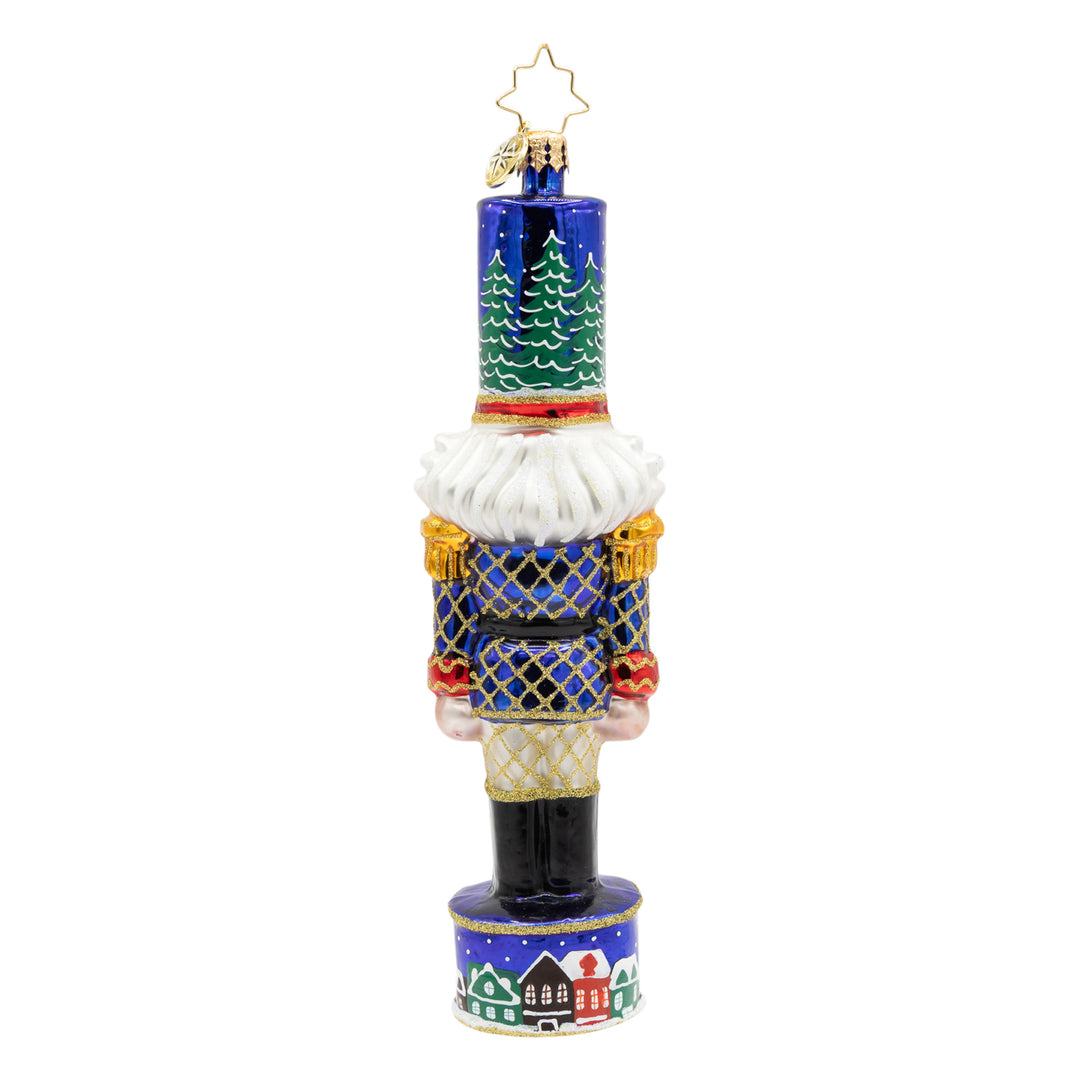 Christmas Sentinel nutcracker ornament in royal blue with gold glitter and snowy village details.