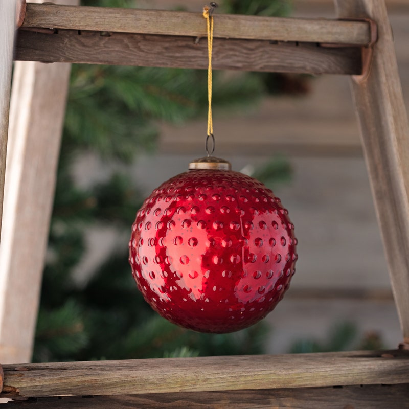 Round 6-inch ruby red mercury glass ornament with a vintage hobnail texture hanging from a string.