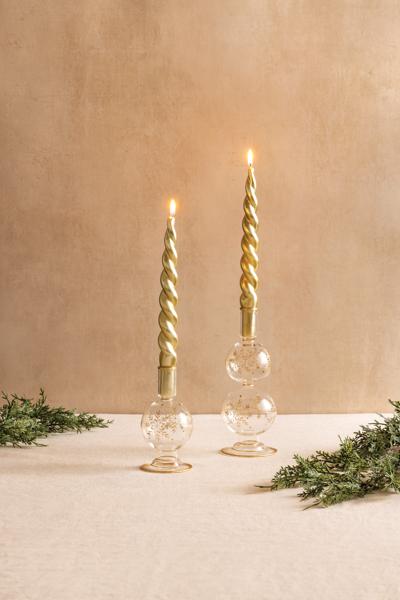 Two glass snowflake taper holders with gold foil details and lit gold spiral candles on a table.
