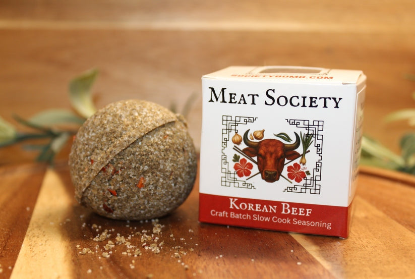 A spherical Korean Beef seasoning bomb next to its white and red Meat Society packaging box.