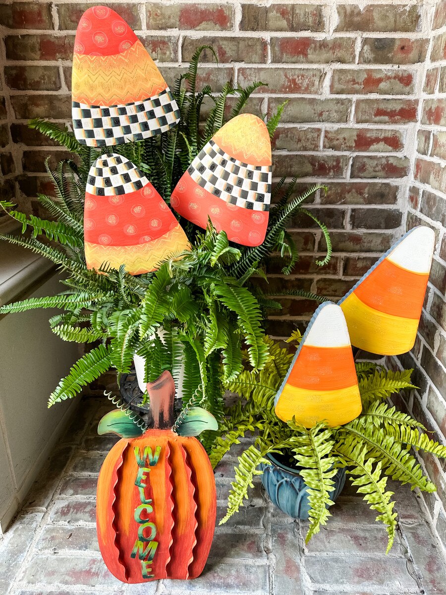 Glittered candy corn garden stakes with checkered patterns and a metal welcome pumpkin on a porch.