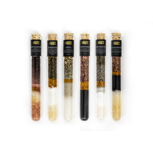 Six glass test tubes filled with layered colorful soaking salts and dried botanicals.