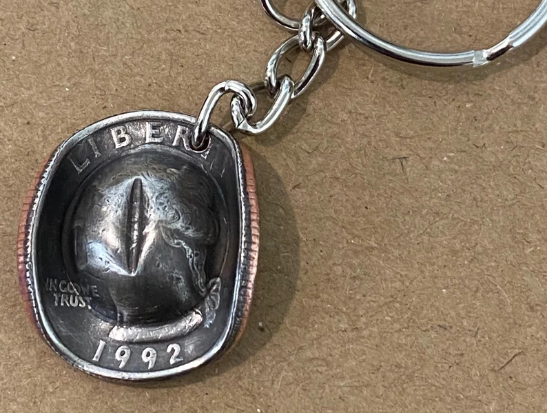 Cowboy hat keychain made from a 1992 US quarter coin on a brown background.