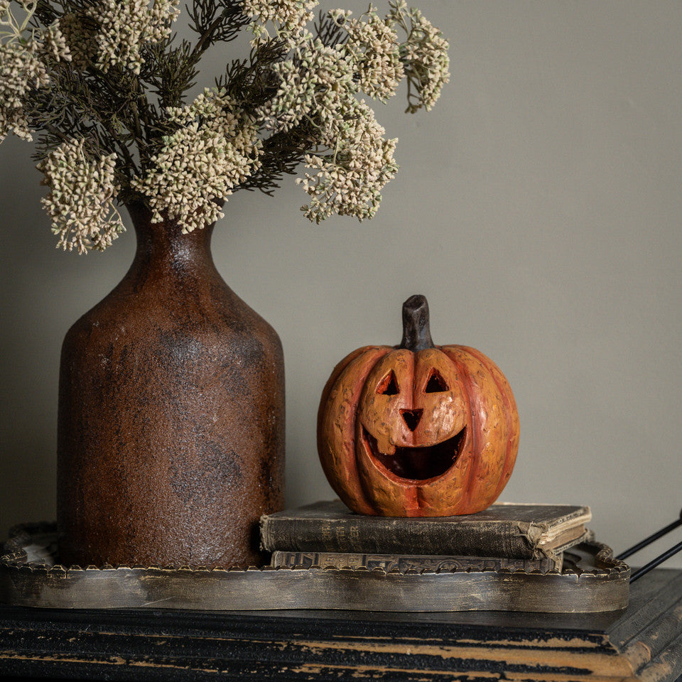 5.5-inch orange mache pumpkin with a large carved grin sitting on vintage books next to a brown vase