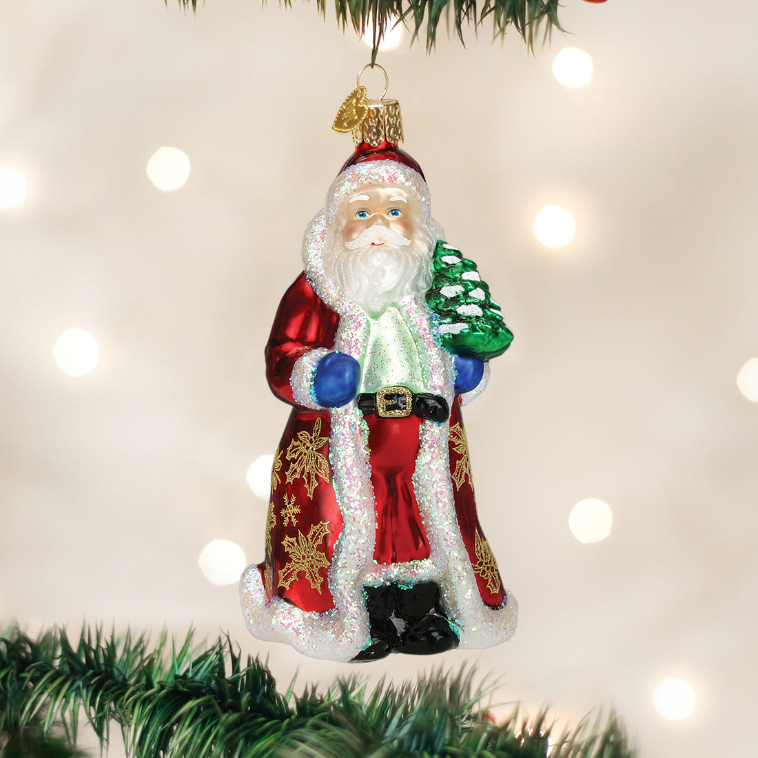 Glistening Golden Santa glass ornament in a red coat with gold patterns, holding a green tree.
