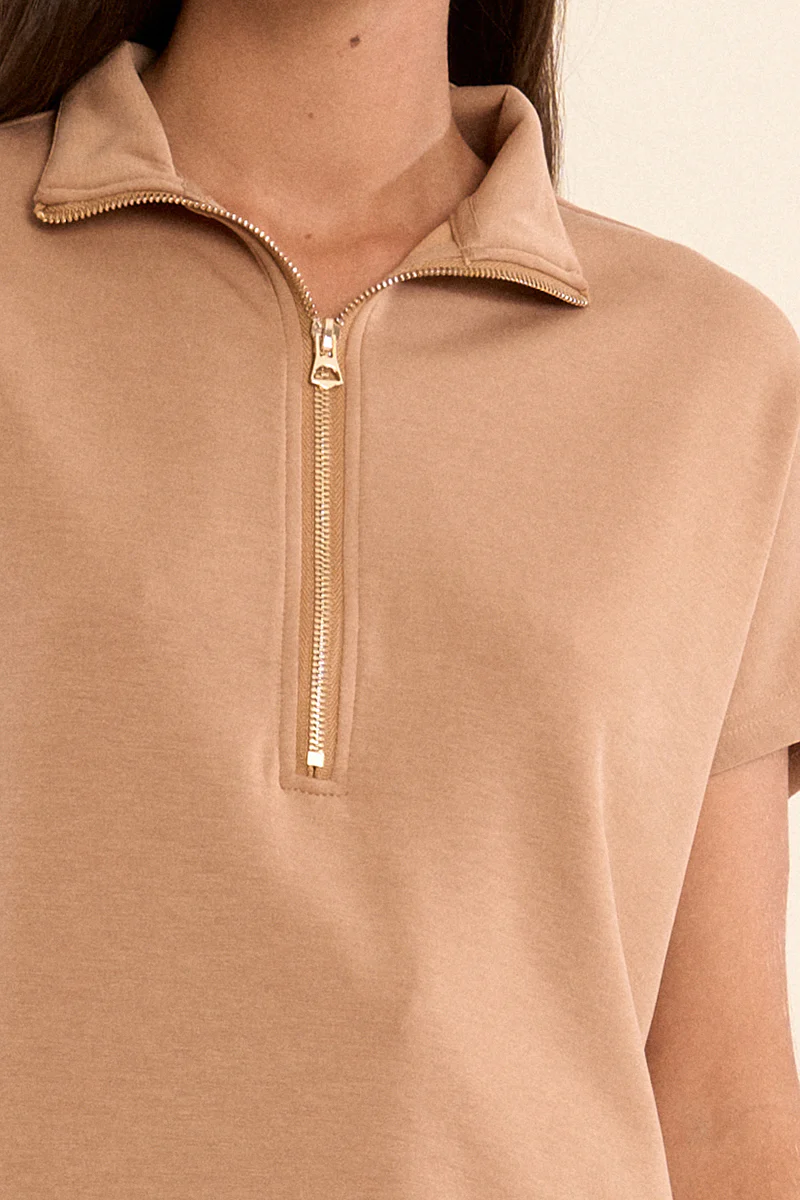 Close-up of a tan sleeveless knitted sweat top with a gold quarter-zip and collar.