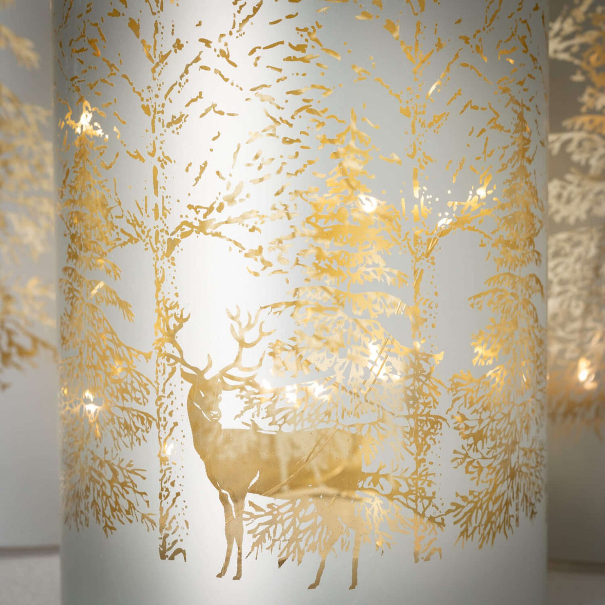 Close-up of a frosted glass cylinder with a gold winter scene featuring a deer and trees.