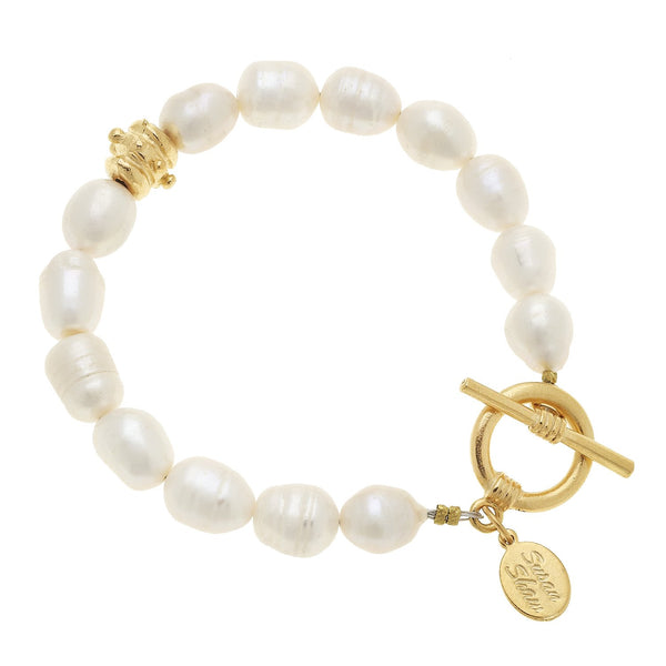 Pearl bracelet with irregular white pearls, a gold toggle clasp, and a small gold logo charm.