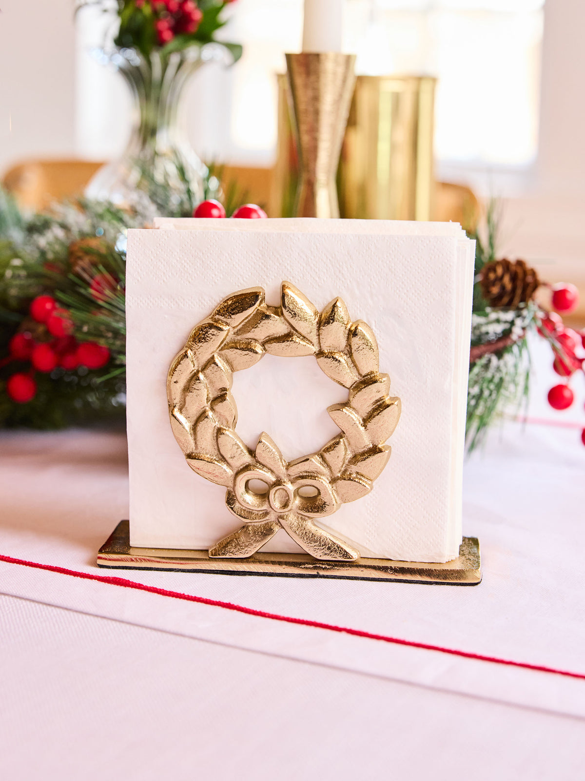 Gold laurel wreath napkin holder with white napkins on a table with festive decor.