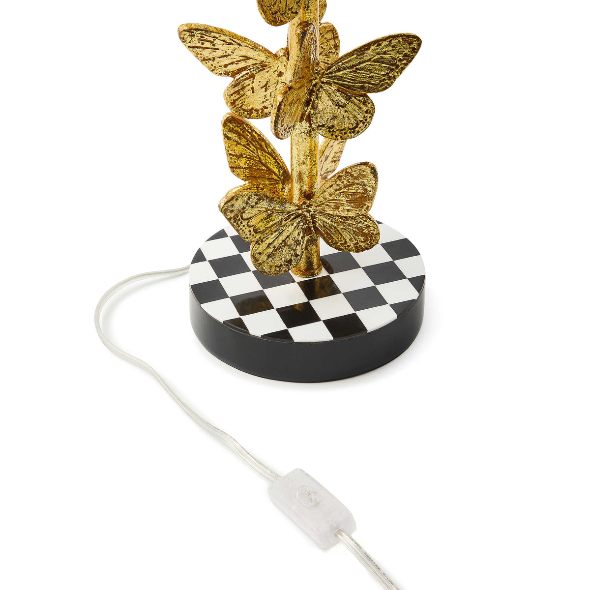 Close-up of a gold butterfly lamp base on a black and white checkered stand with a clear power cord.