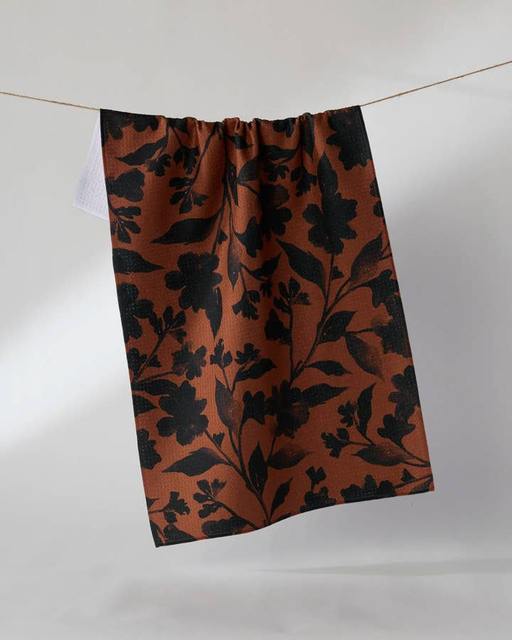 Halloween tea towel with a black floral silhouette pattern on a rust-brown waffle weave fabric.