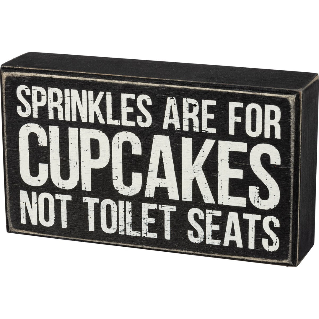 Black wooden box sign with white distressed text that reads "SPRINKLES ARE FOR CUPCAKES NOT TOILET SEATS".