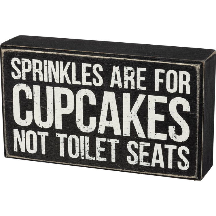 Black wooden box sign with white distressed text that reads "SPRINKLES ARE FOR CUPCAKES NOT TOILET SEATS".