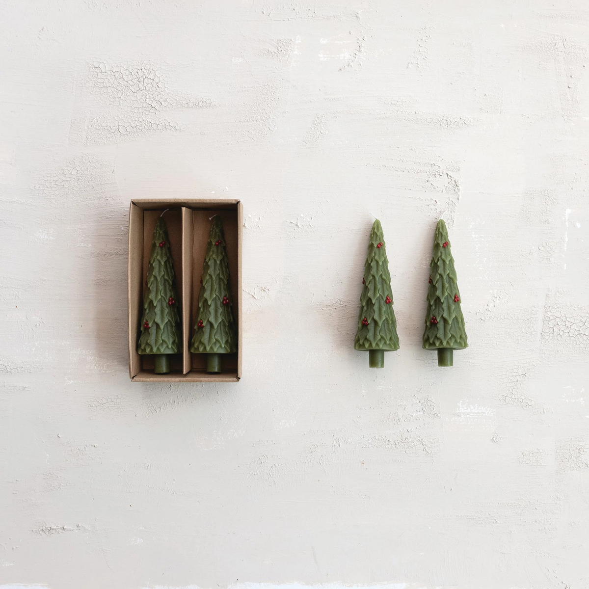 Four green unscented tree-shaped taper candles, two in a brown box and two standing beside it.