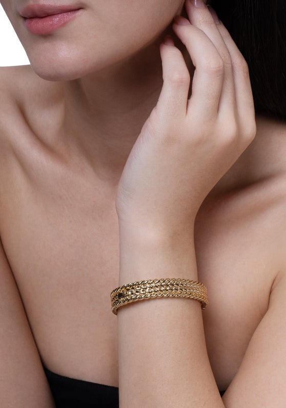 A person wearing the thick Cheval Braid Hinged Bangle in 18K gold plated brass on their wrist.