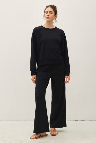 Woman wearing a black Terry Brushed Sweatshirt with matching wide-leg pants and tan sandals.