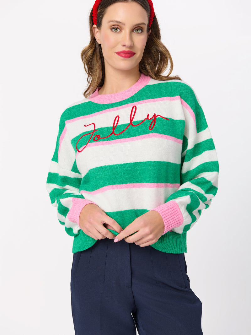 Woman wearing the Jolly Stripe Relaxed Sweater in green, pink, and cream with red script embroidery.