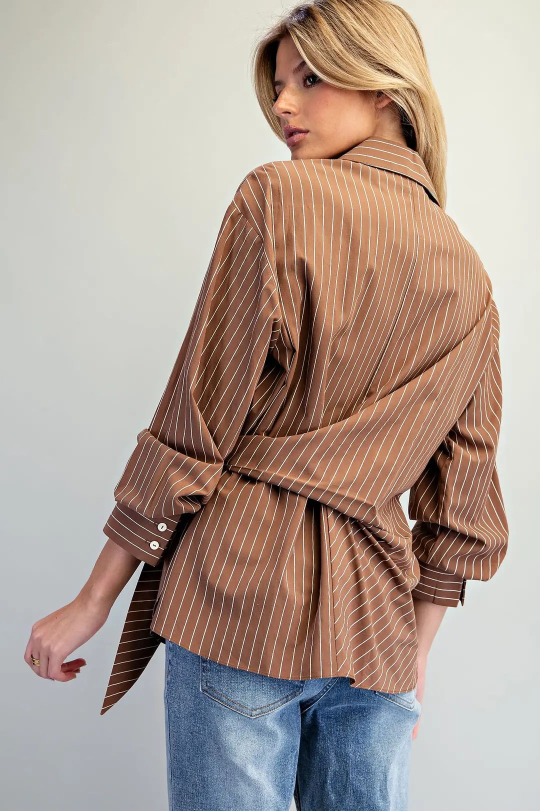 Back view of a brown pinstriped Reese Tie Waist Blouse with a wrap-around tie and buttoned cuffs.
