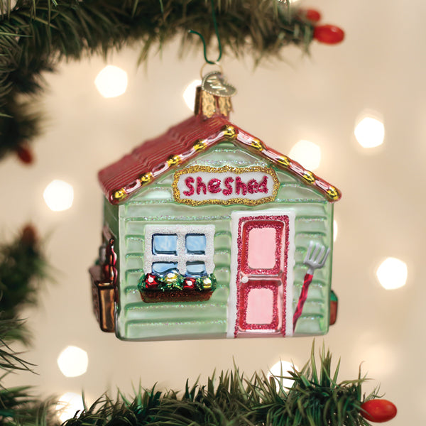 Glass She Shed Christmas ornament with a red roof, green siding, and pink door on a tree.