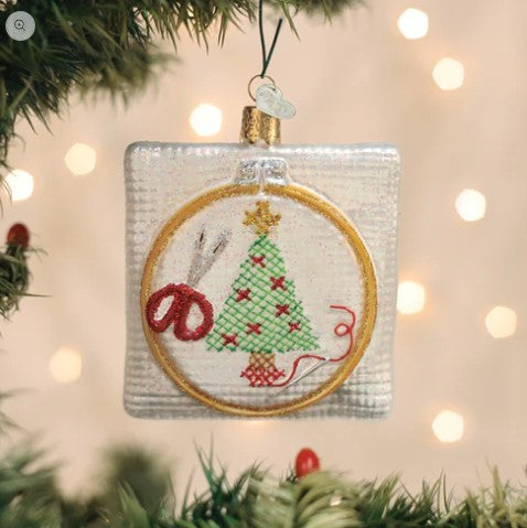 Square glass Christmas cross stitch ornament featuring a tree, scissors, and needle in a hoop.
