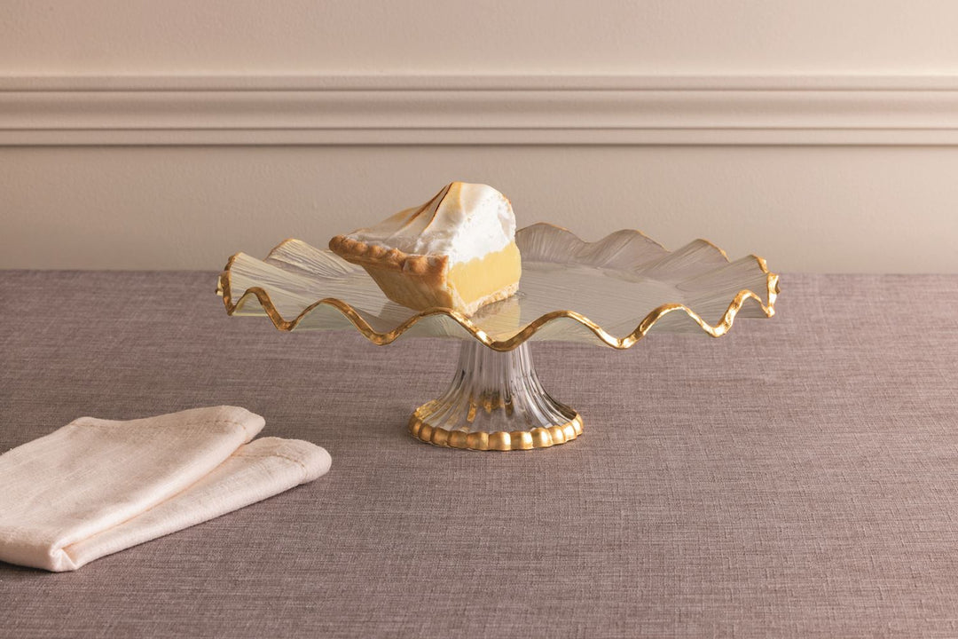 Glass cake stand with a gold foil ruffle edge and pedestal, holding a slice of lemon meringue pie.