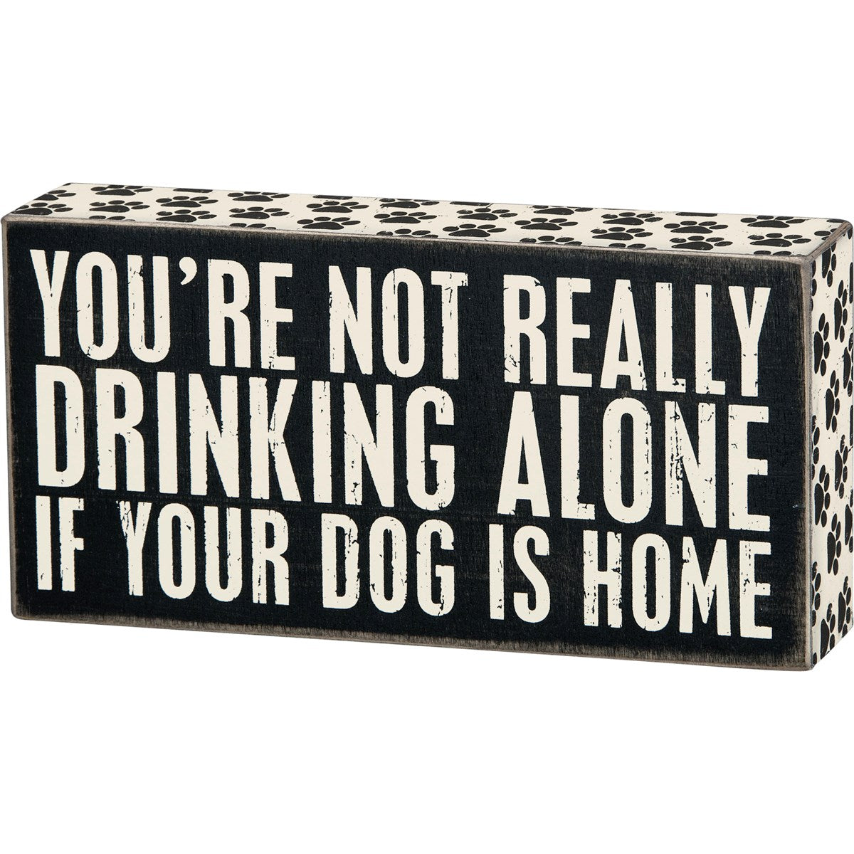 Black wooden box sign with white text reading "YOU'RE NOT REALLY DRINKING ALONE IF YOUR DOG IS HOME". Paw print pattern on top and sides.