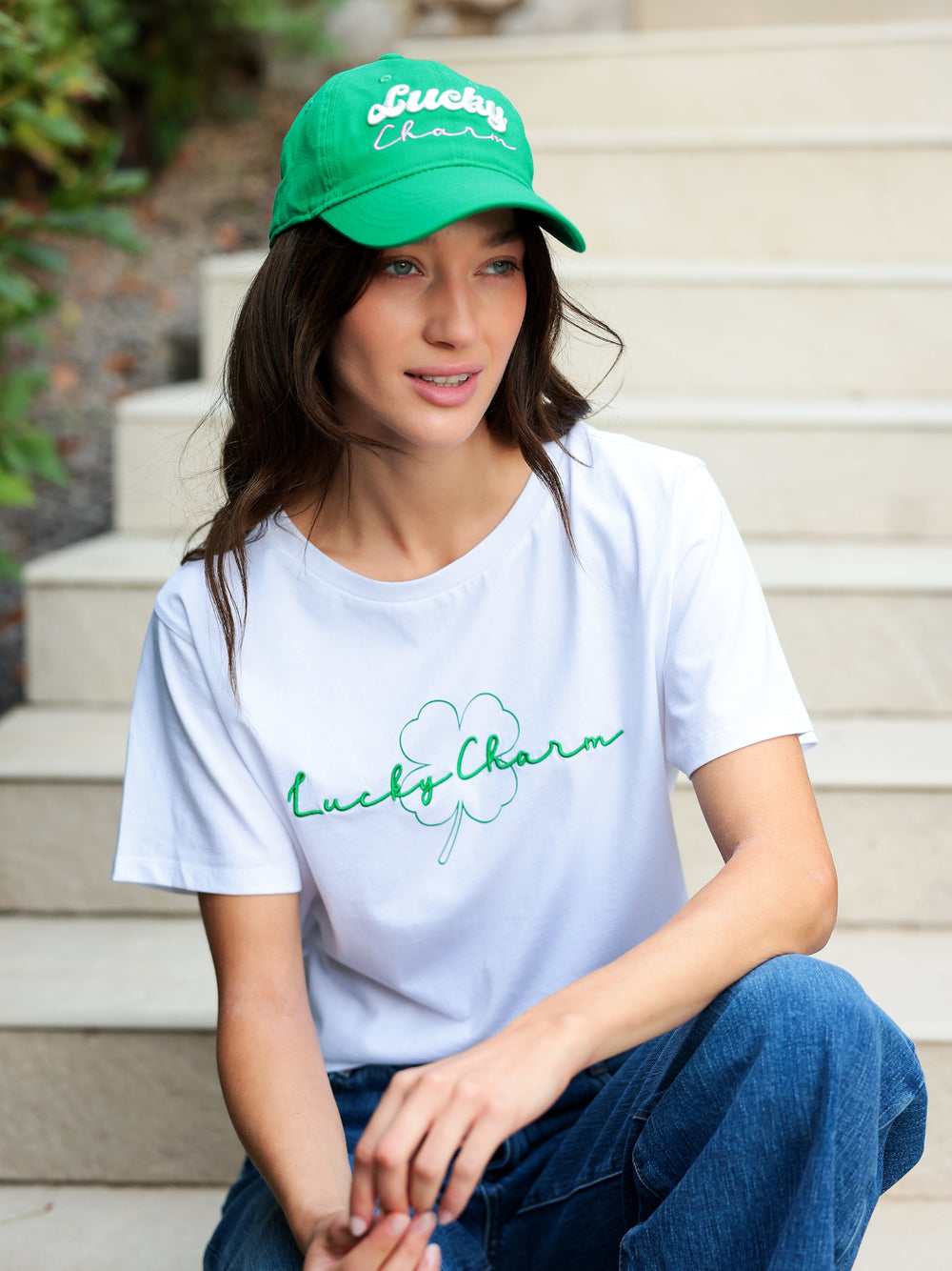 Woman wearing a white Hannah Lucky Charm T-shirt with green embroidered clover and script.