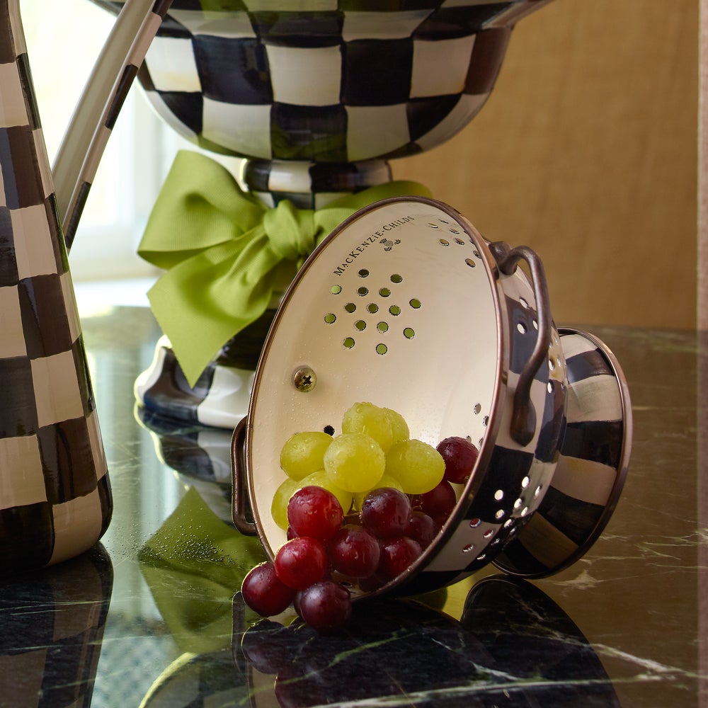Small Courtly Check Enamel Colander with red and green grapes on a dark marble countertop.