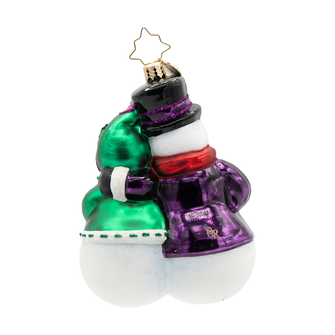 Glass ornament of two snowmen hugging, wearing a green coat and a purple coat with a black top hat.