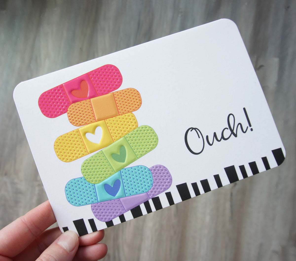 Die-cut get well card shaped like a bandage with embossed text reading Ouch inside and Hope your boo-boo feels better soon.