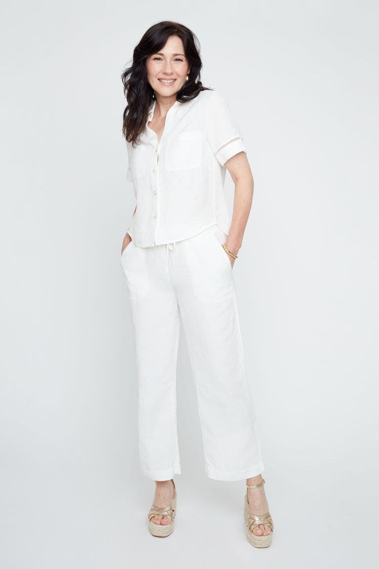 Woman in a white linen short-sleeve button-up blouse and matching wide-leg pants, wearing gold espadrille wedges.