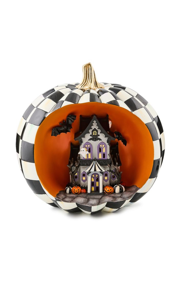 Illuminated black and white checkered pumpkin shell containing a miniature haunted house scene.