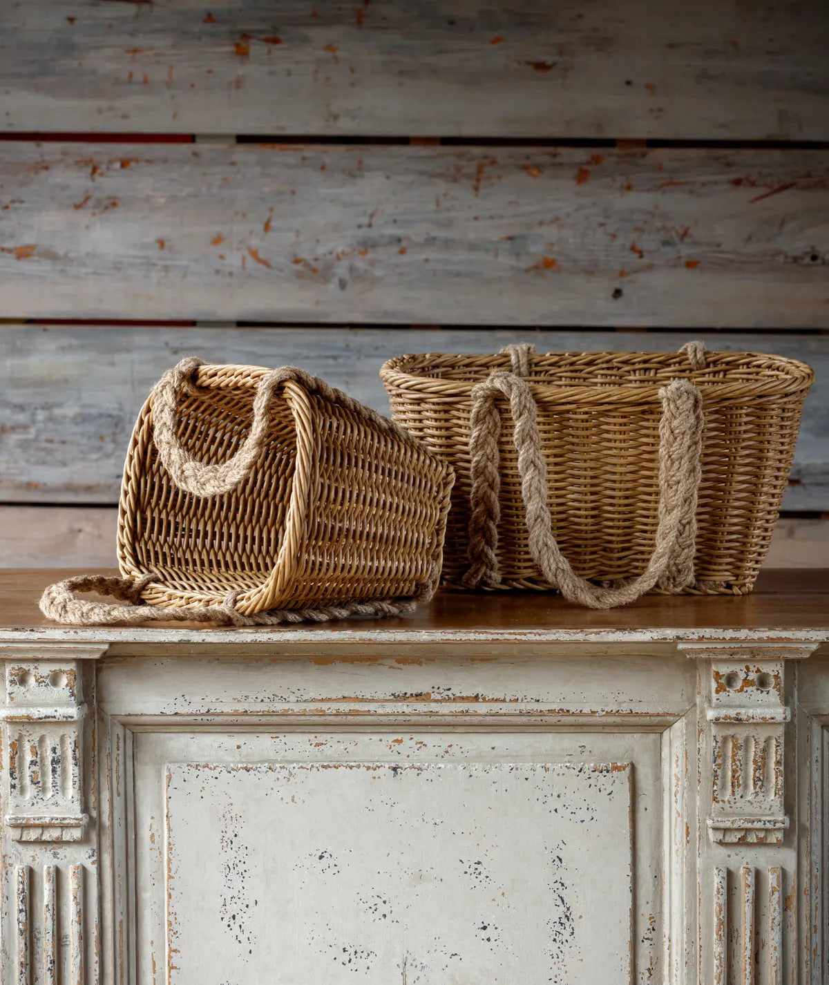 Two woven poly baskets with braided rope handles on a distressed white cabinet.