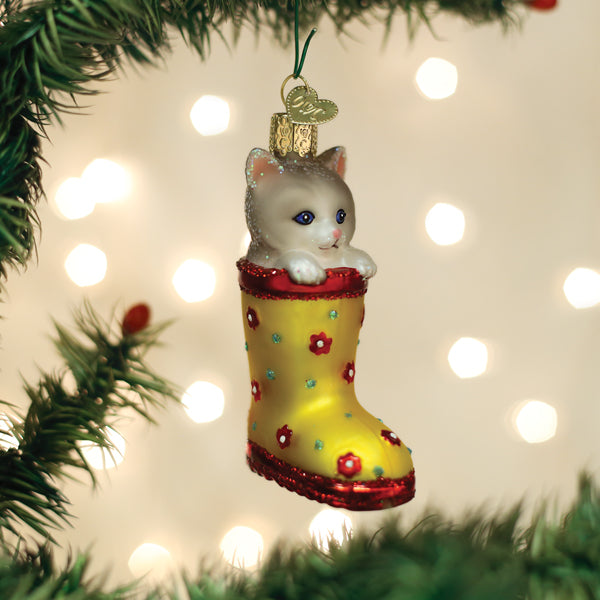 Glass Christmas ornament featuring a white kitten peeking out of a yellow rain boot with red trim.