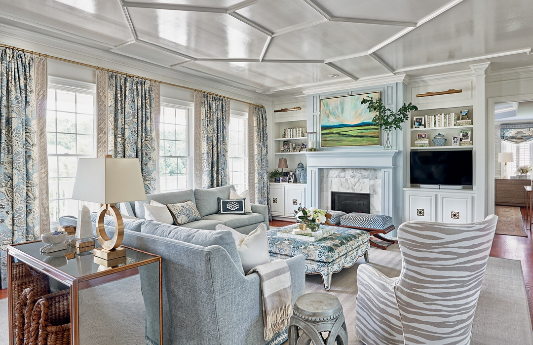Southern Sensibility living room with blue sofas, patterned ottoman, and coffered ceiling.