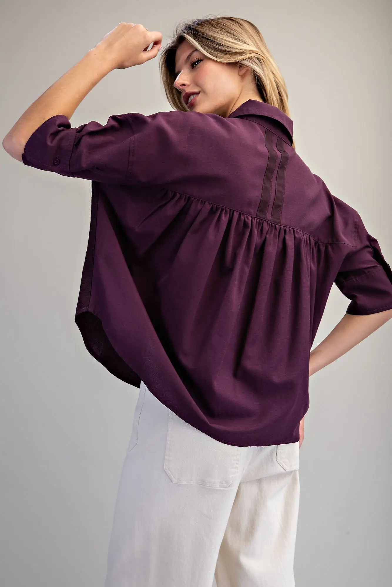 Back view of a woman wearing a plum purple oversized button-up shirt with pleated back detailing.