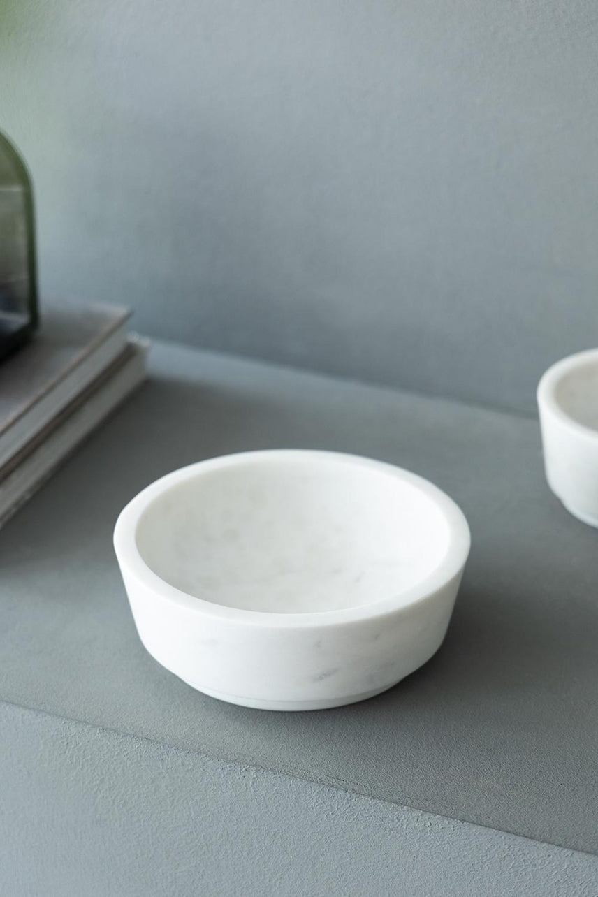 Round white marble bowl on a grey surface next to books.
