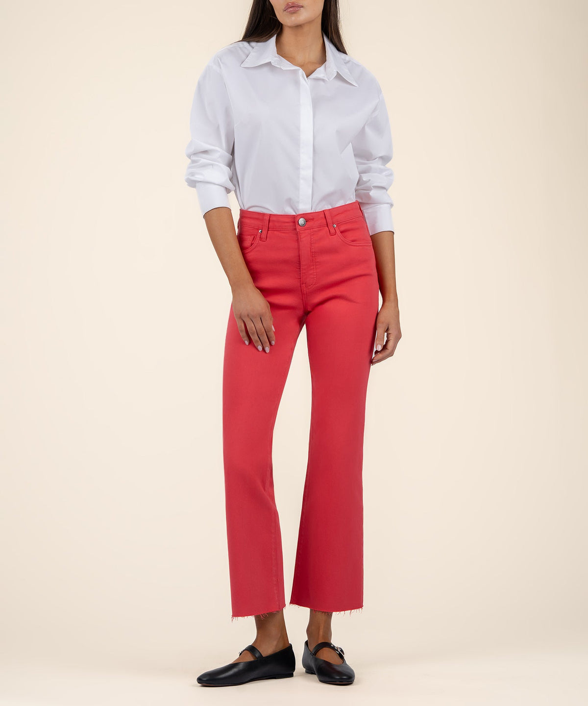 Woman wearing Kelsey high rise ankle flare jeans in coral red with a raw hem and white button-down.