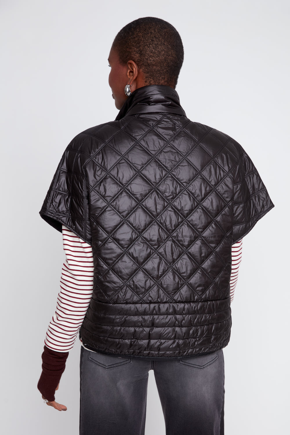 Back view of a woman wearing a black Megan Luxe Quilted Poncho over a striped long-sleeve shirt.
