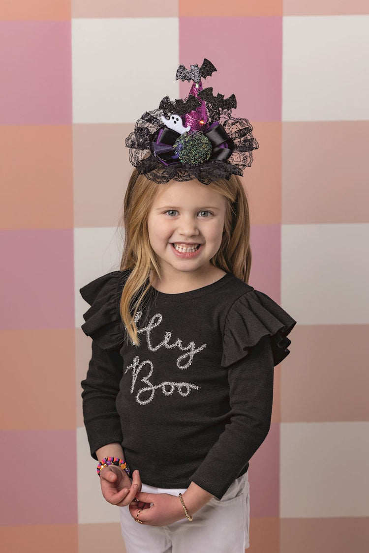 Young girl wearing a Halloween light-up headband with a purple glitter hat, bats, and black lace.