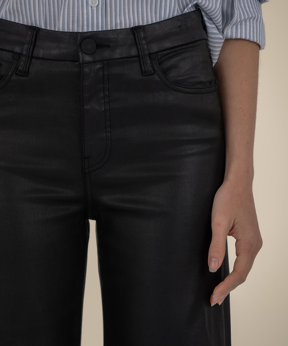 Close-up of black high-rise wide-leg pants with a coated finish and front pocket details.