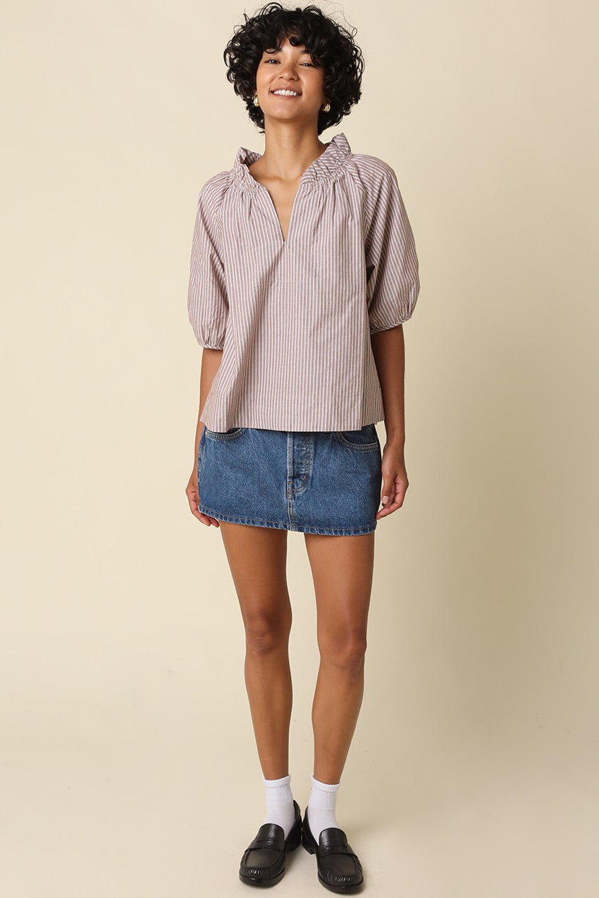 Woman wearing the Evan Stripe Puff Sleeve Blouse in a brown and white stripe with a denim mini skirt.