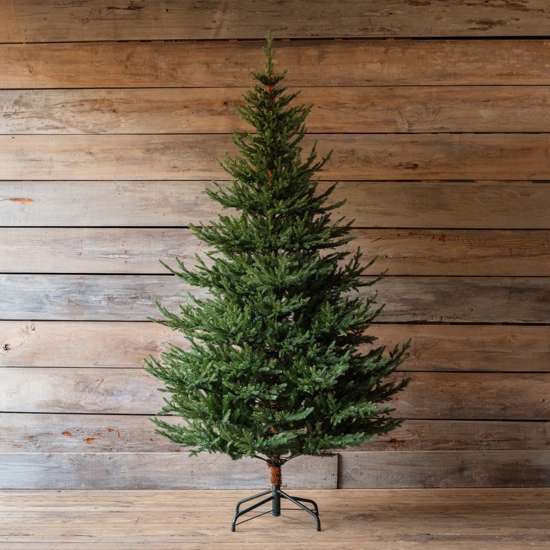 Olympia Fir 5 Ft artificial Christmas tree with green needles and a metal stand against wood walls.