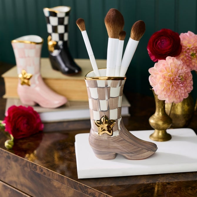 Mocha check cowboy boot bud vase holding makeup brushes on a white marble block.