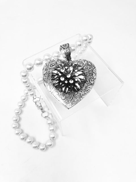 Fashion pearl necklace featuring an intricate silver heart pendant locket with a floral design.